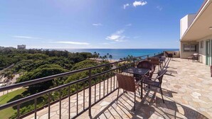 Ein Balkon mit Blick auf den Ozean und einen Strand, möbliert mit Korbstühlen und einem Tisch.