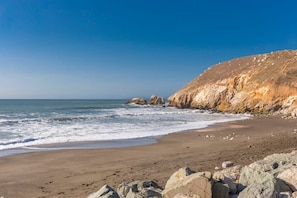 Une plage avec des affleurements rocheux, une étendue de sable et un ciel bleu dégagé.