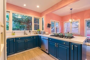 Une cuisine avec des armoires de couleur turquoise, un plan de travail blanc et une grande fenêtre.