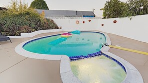 Una piscina con borde de azulejos azules, un jacuzzi y un flotador inflable pequeño.