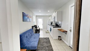 A narrow hallway with a blue sofa, a small table, and a rug. There is a kitchen area with cabinets and a microwave. - Cool New Remodel Near Coronado, NEW Jacuzzi, Fire Pit, BBQ, Walk to Downtown! (San Diego)
