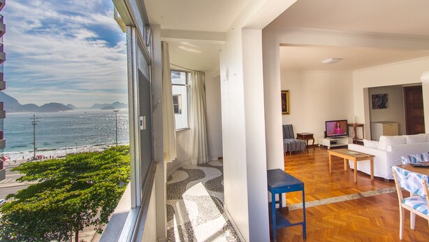 A balcony with a view of the sea and mountains, a living room with a sofa and TV, and a dining area with a table and chairs. - LineRio Vista Mar Copacabana 228 (Rio de Janeiro)