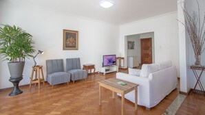 A living room with a white sofa, striped chairs, a wooden coffee table, a television, a potted plant, and a painting on the wall. - LineRio Vista Mar Copacabana 228 (Rio de Janeiro)
