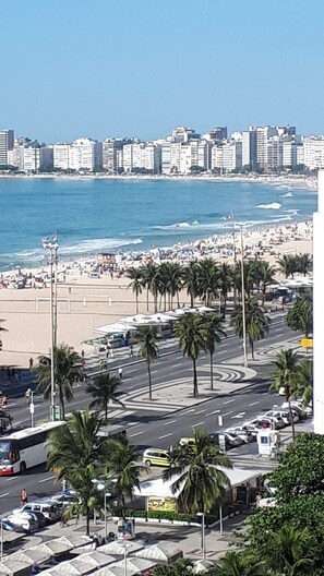 A coastal cityscape with a beach, palm trees, and a road with vehicles.