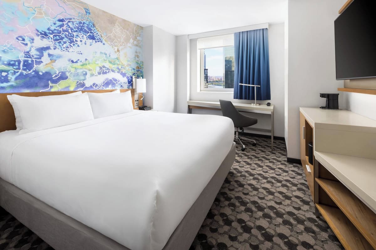 A hotel room with a large bed, a desk, a chair, and a TV.