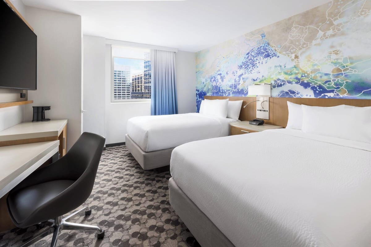 A hotel room with two beds, a desk, a chair, a TV, and a window with curtains.