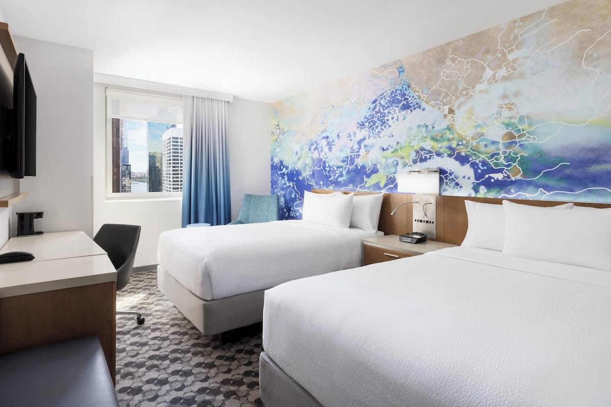 A hotel room with two beds, a desk, a chair, a TV, and a large abstract painting on the wall.