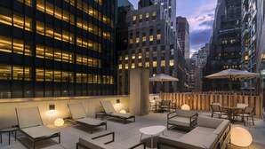 A rooftop lounge with outdoor seating, including lounge chairs and tables, and umbrellas providing shade. - Courtyard by Marriott New York Downtown Manhattan/Financial District (New York)