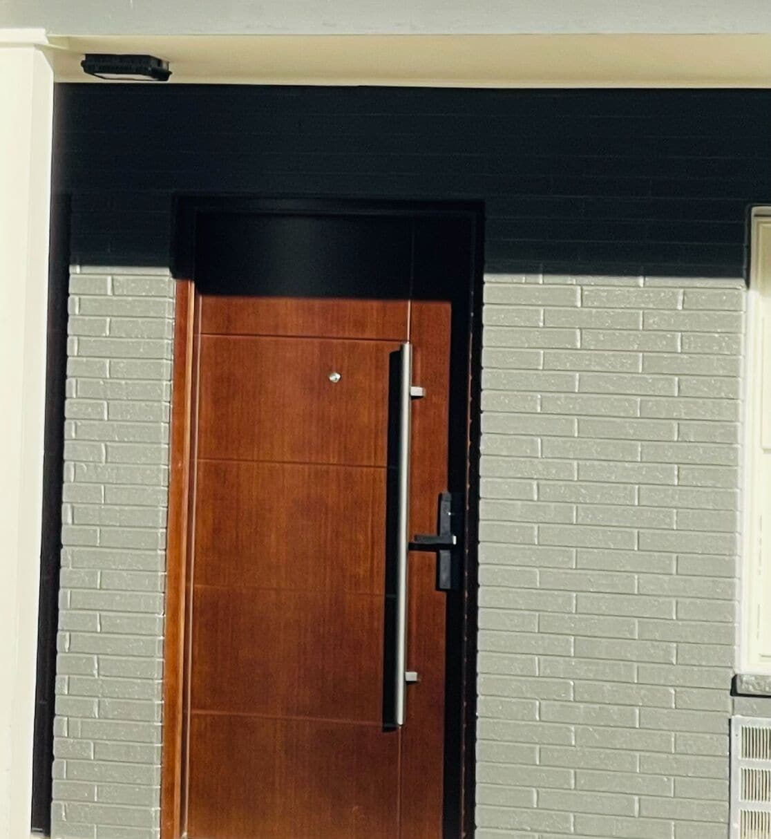 A wooden door with a black frame and a vertical handle, set in a building with white brick walls.