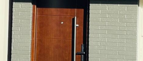 A wooden door with a black frame and a vertical handle, set in a building with white brick walls.