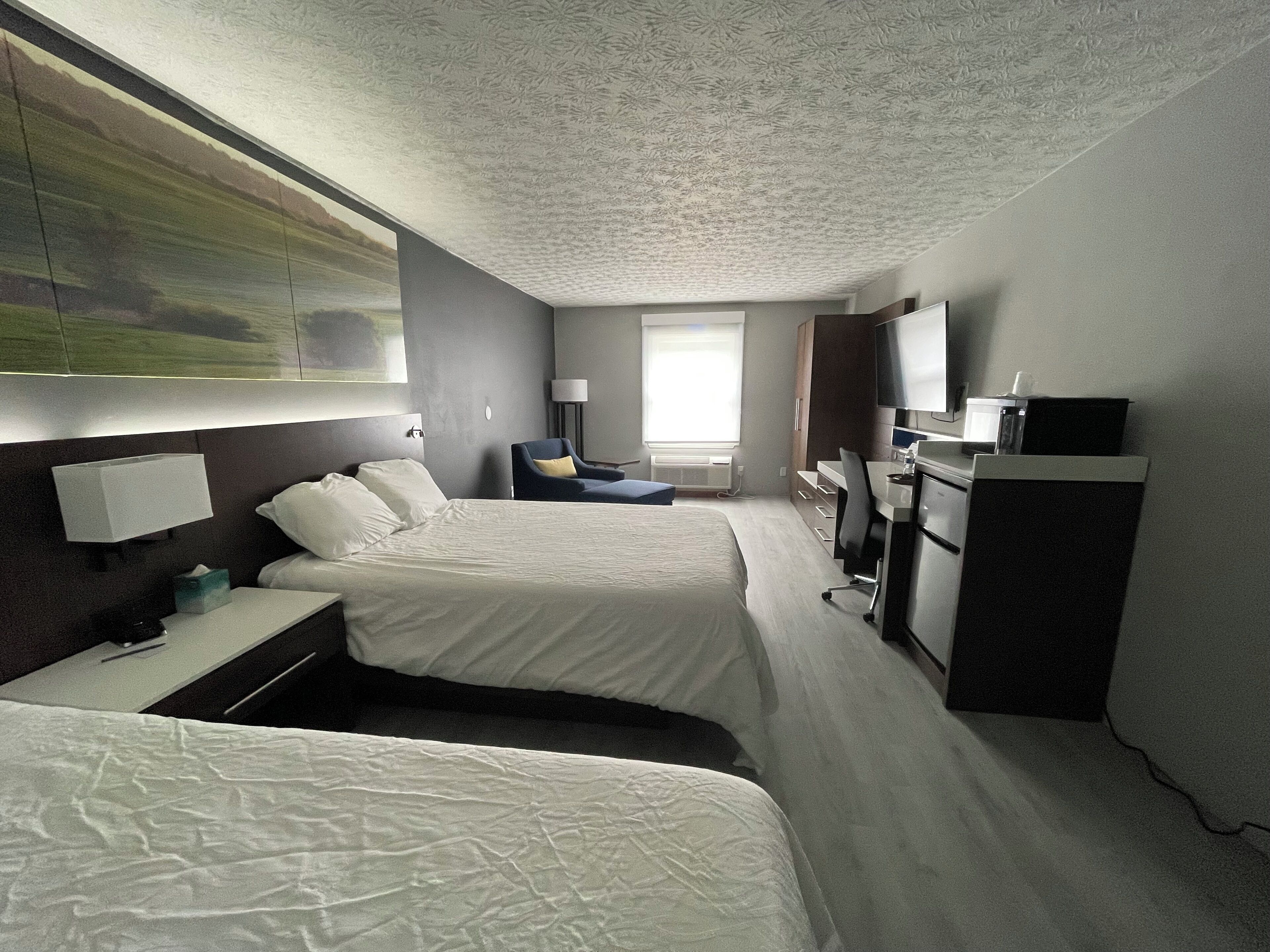 A hotel room with two beds, a desk, a chair, a TV, and a large window.