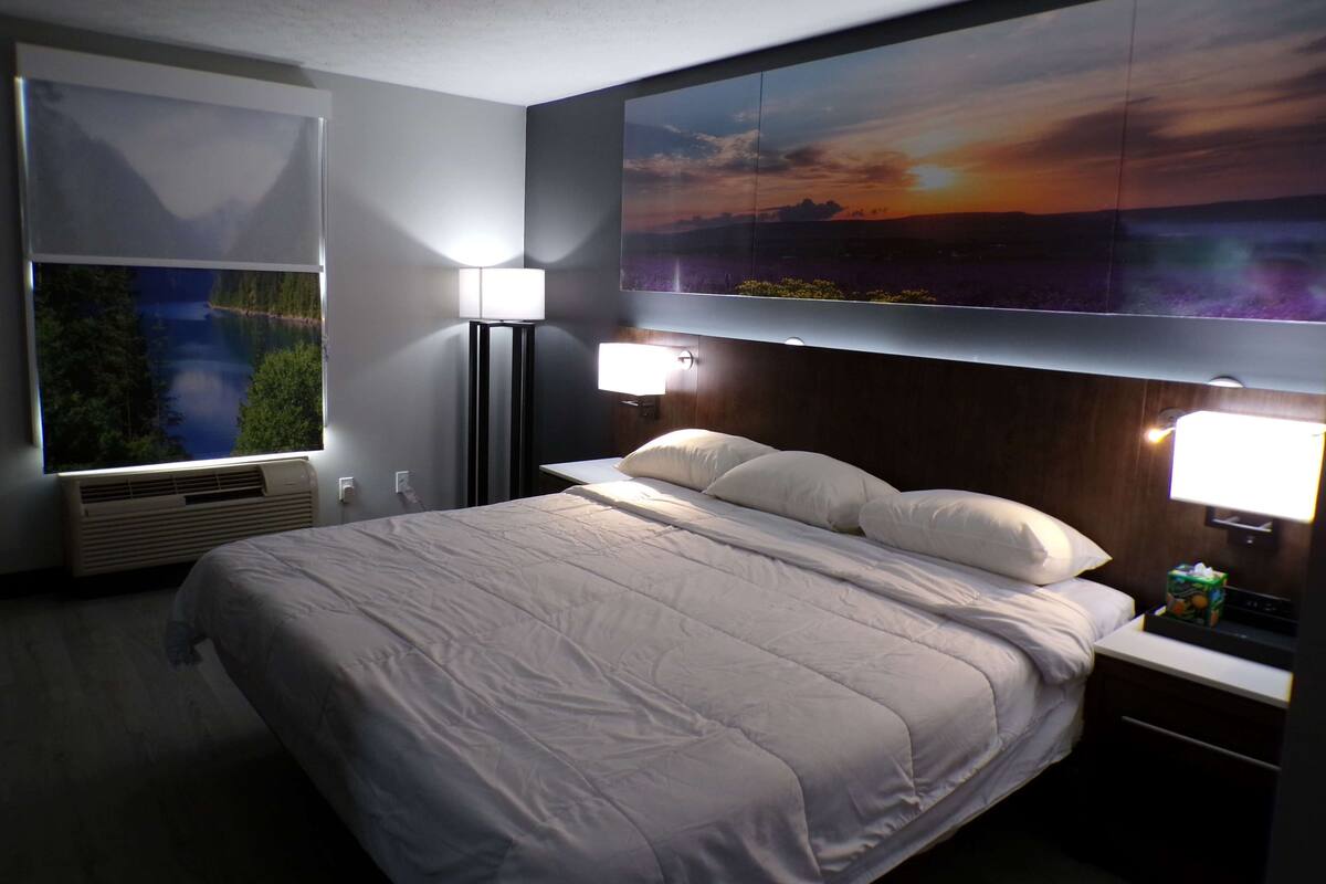 A hotel room with a large bed, two bedside lamps, a nightstand, and a wall-mounted TV displaying a scenic landscape.