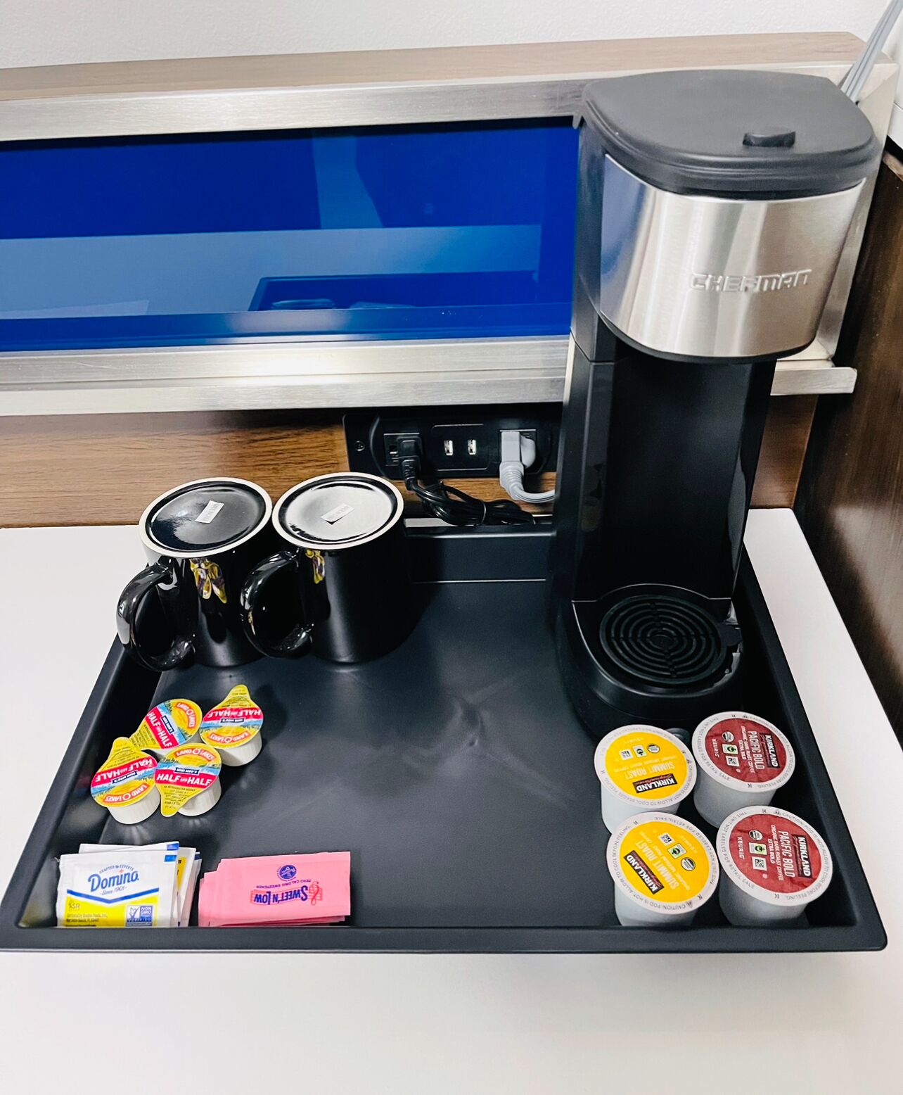 A coffee station with a coffee maker, milk frothing machine, and various milk and creamer containers.