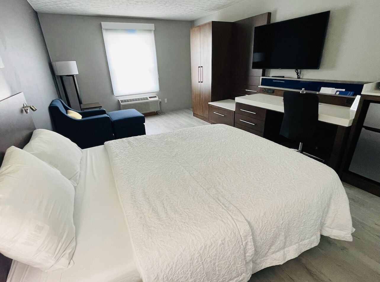 A hotel room with a bed, a desk, a chair, a television, and a window.