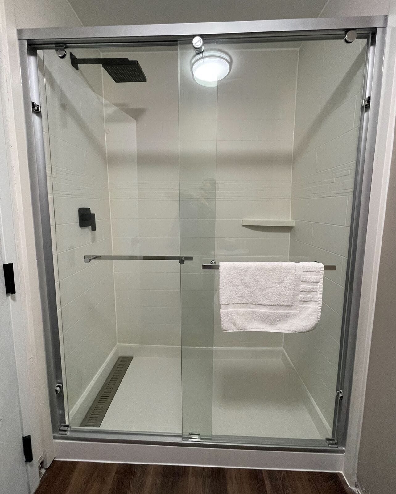 A glass-enclosed shower with a white towel hanging on a rack.