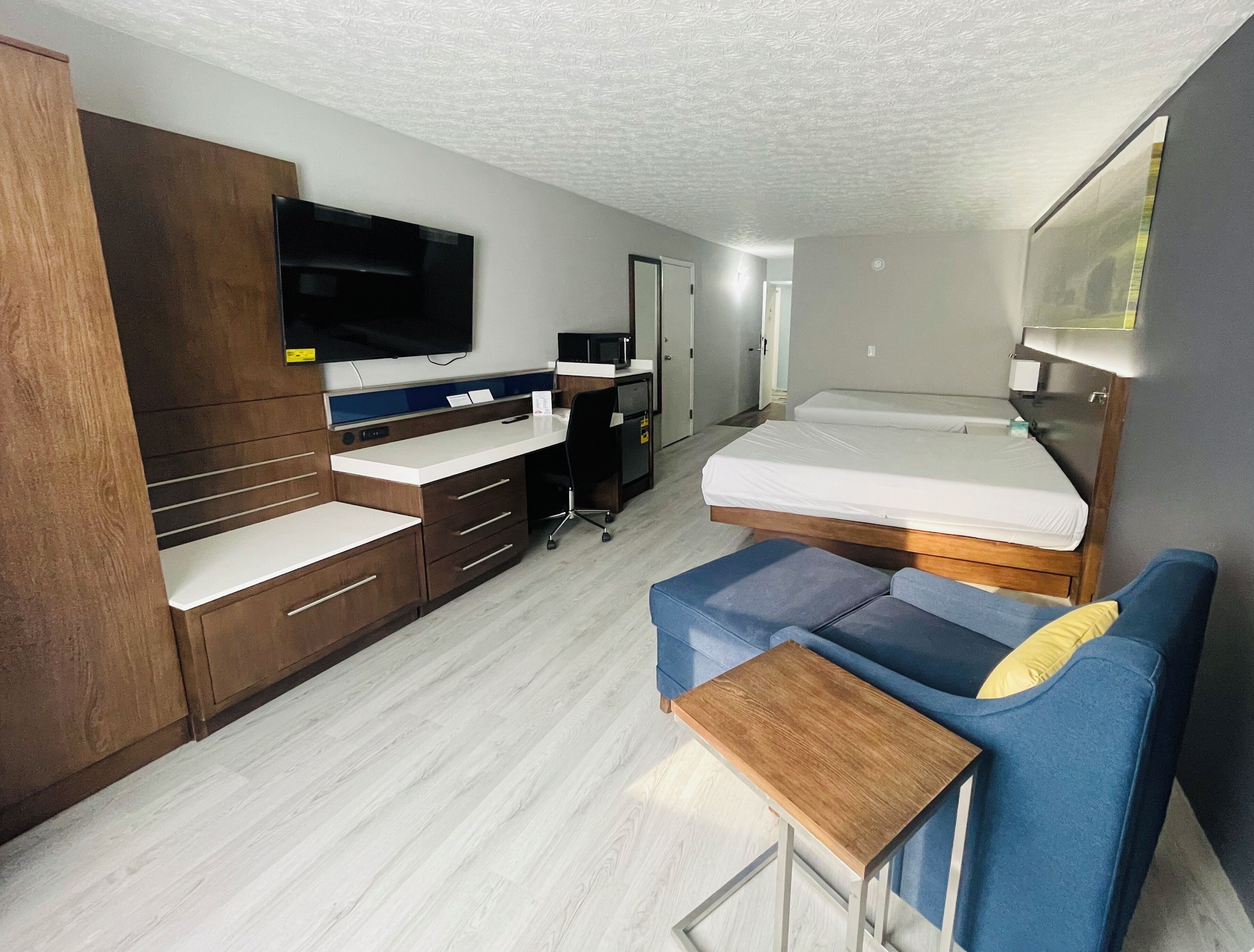 A compact hotel room with a kitchenette, a bed, a sofa, and a TV.