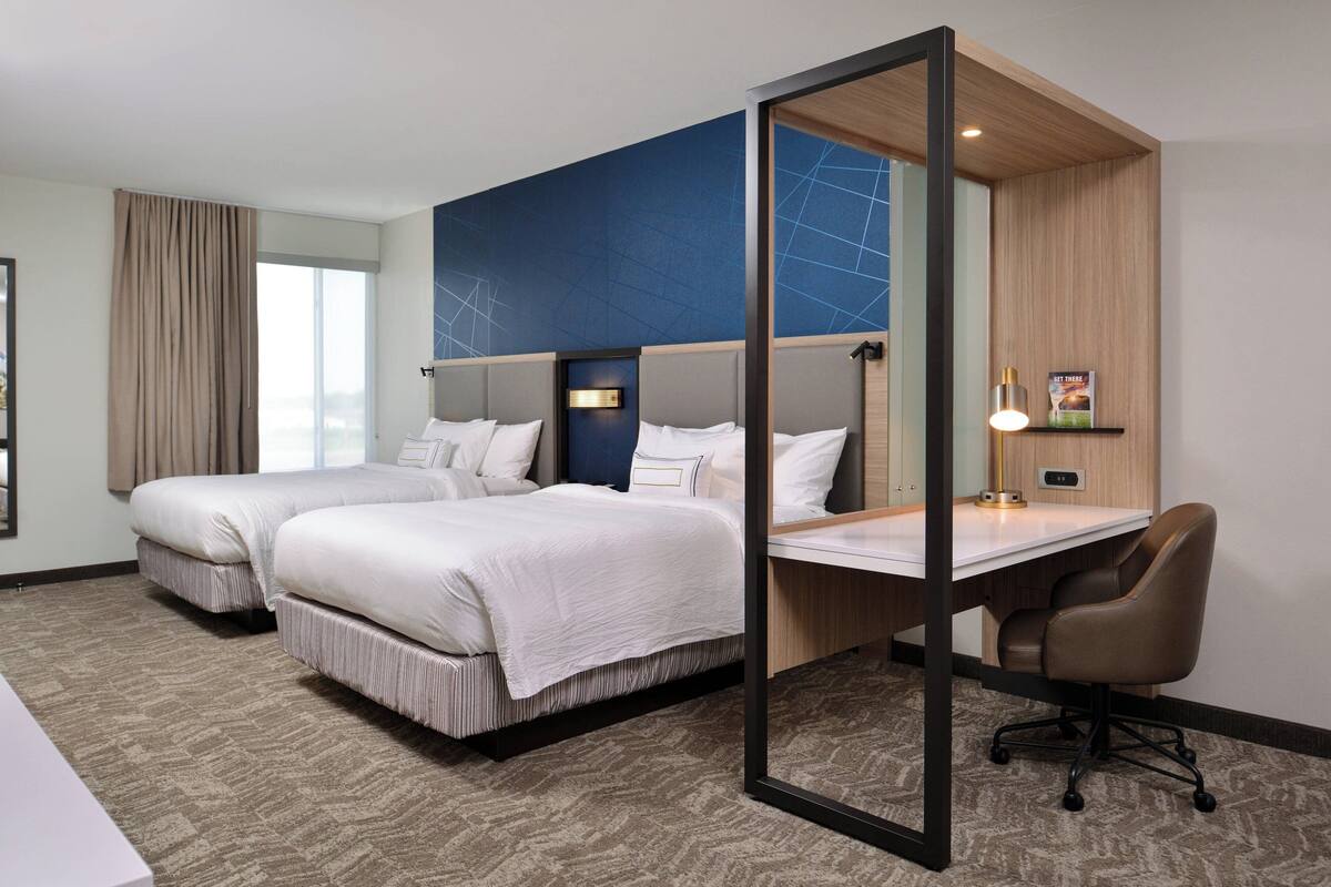 A hotel room with two beds, a desk, and a chair.