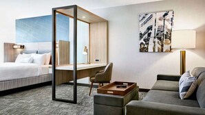 Une chambre d’hôtel avec un lit, un bureau, une chaise, un canapé et un tableau au mur.