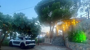 A white car parked in a driveway with a stone wall and a pergola with lights. - Family friendly house close to the beach (Κριθάρια)