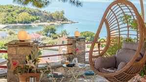 A wicker chair with a cushion, a small table with a book, a metal watering can, and a potted plant with flowers. - Family friendly house close to the beach (Κριθάρια)