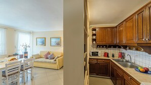 A modern kitchen with wooden cabinets, a sink, and a microwave. There is a dining area with a table and chairs, and a sofa. - Family friendly house close to the beach (Κριθάρια)