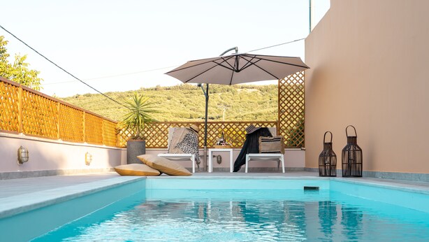 Une piscine dotée de chaises longues et d’un parasol, entourée d’une clôture en bois et offrant une vue sur un paysage vallonné.