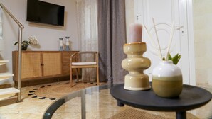 Un salon moderne avec une table basse en verre, un fauteuil en osier, un téléviseur fixé au mur et une porte à cadre blanc.