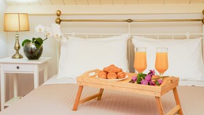 Un lit bien fait, avec du linge de lit blanc, une table de chevet avec une lampe et un vase de fleurs, et un plateau avec des croissants et du jus d’orange posé sur le lit.