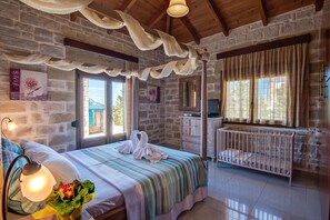 A cozy room with a bed, a crib, and a stone wall. - HECTORAS VILLA in Plaka-BY APOKORONAS VILLAS (Πλάκα)