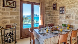 A dining area with a stone wall, a table set for breakfast, and a wine rack. - HECTORAS VILLA in Plaka-BY APOKORONAS VILLAS (Πλάκα)