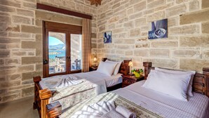 A room with two beds, wooden headboards, stone walls, and a view through a door. - HECTORAS VILLA in Plaka-BY APOKORONAS VILLAS (Πλάκα)