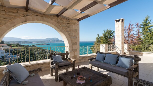A terrace with stone arches, wooden furniture, and a view of the sea. - HECTORAS VILLA in Plaka-BY APOKORONAS VILLAS (Πλάκα)