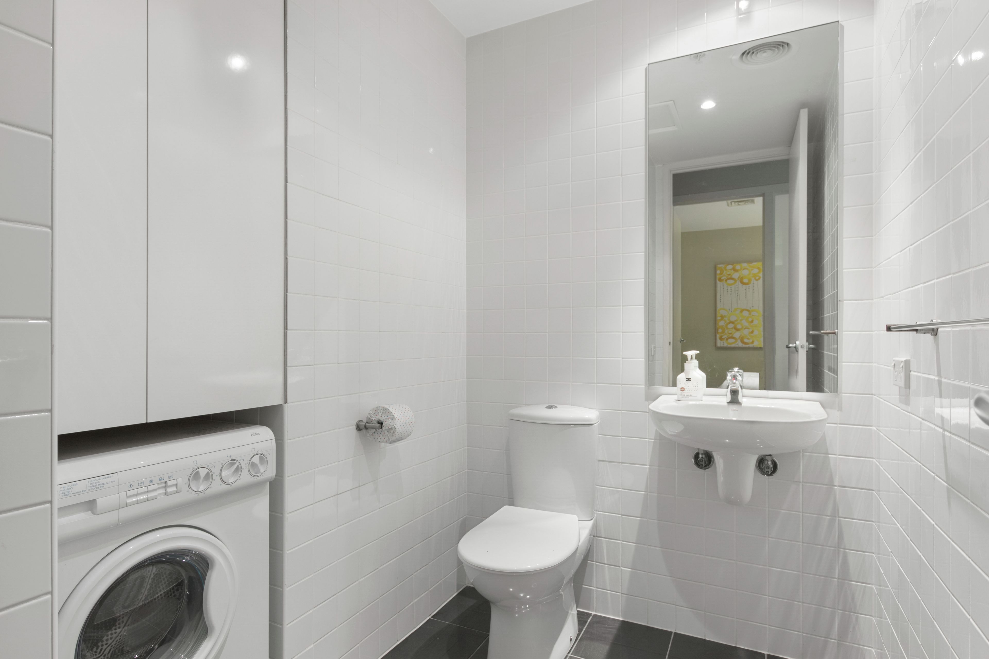 A modern bathroom with a washing machine, toilet, and sink.