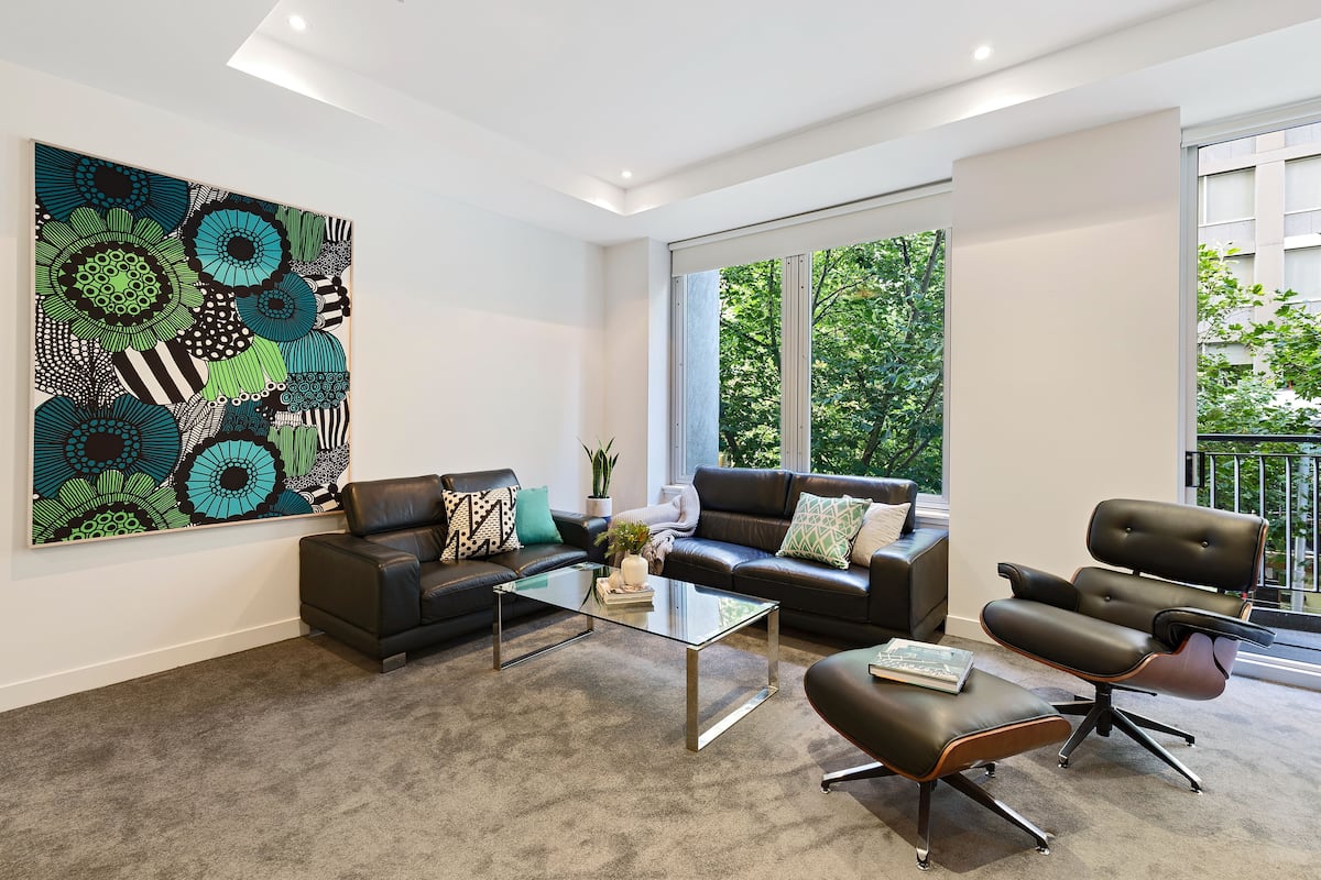 A modern living room with a glass coffee table, leather sofas, and a large abstract painting.