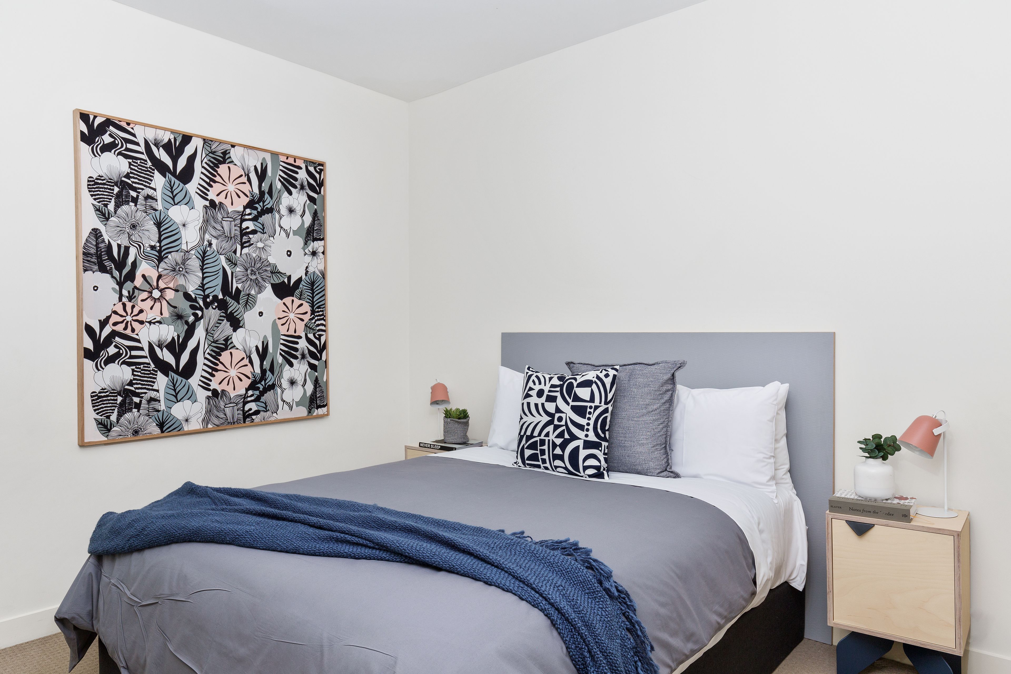 Una camera da letto con un letto, un comodino, una lampada a parete e un'ampia opera d'arte floreale.