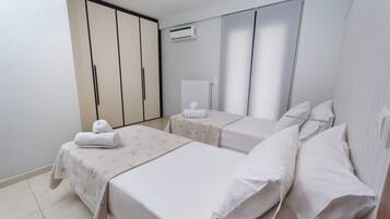 A hotel room with two beds, a wardrobe, an air conditioning unit, and a radiator.