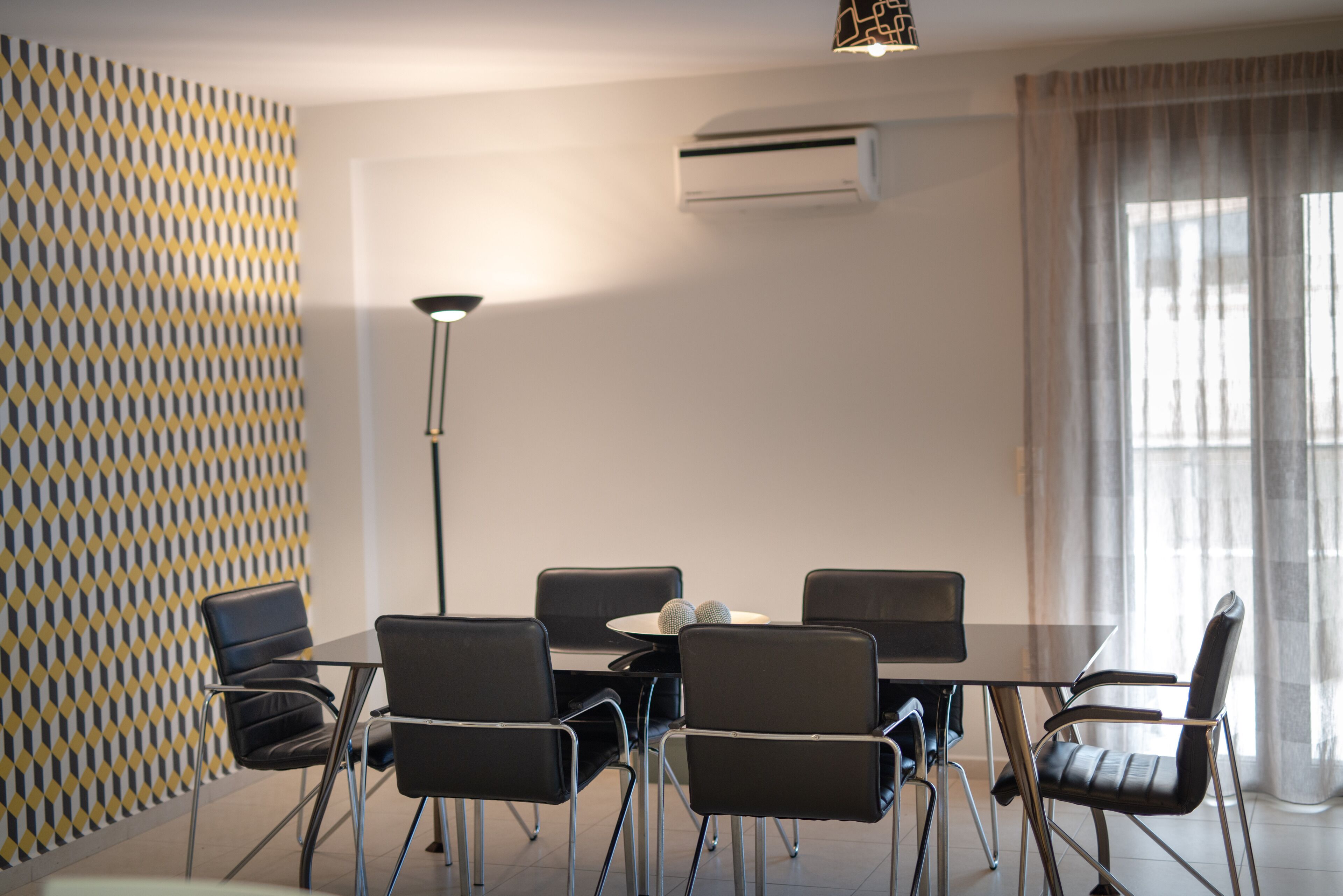 A modern conference room with a geometric patterned wall, a round table with six chairs, and an air conditioning unit on the wall.