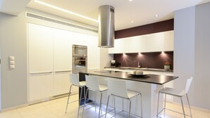 A modern kitchen with white cabinetry, a stainless steel range hood, and a central island with bar stools. - Prime 3BR/2BA Apt Heart of Heraklion-Fiber WIFI–Steps to Lions Sq Walk to Port 2 (Ηράκλειο)