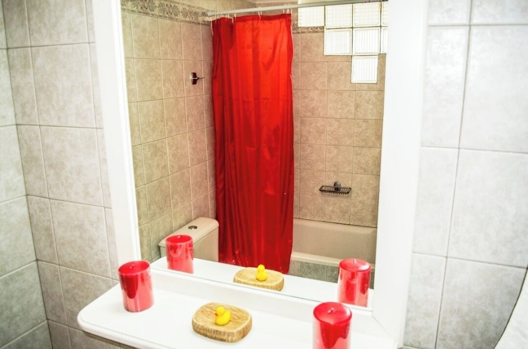 A bathroom with a red shower curtain, a white bathtub, and a sink with red cups and a yellow rubber duck.