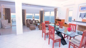 A spacious living area with a glass dining table, red chairs, and a sofa. There is a view of the ocean through large windows. - Villa Sea View (Ρέθυμνο)