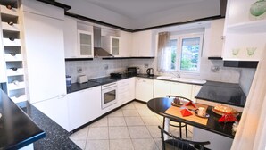 A compact kitchen with white cabinets, a black countertop, a window with a view, and a dining area with a table and chairs. - Villa Sea View (Ρέθυμνο)