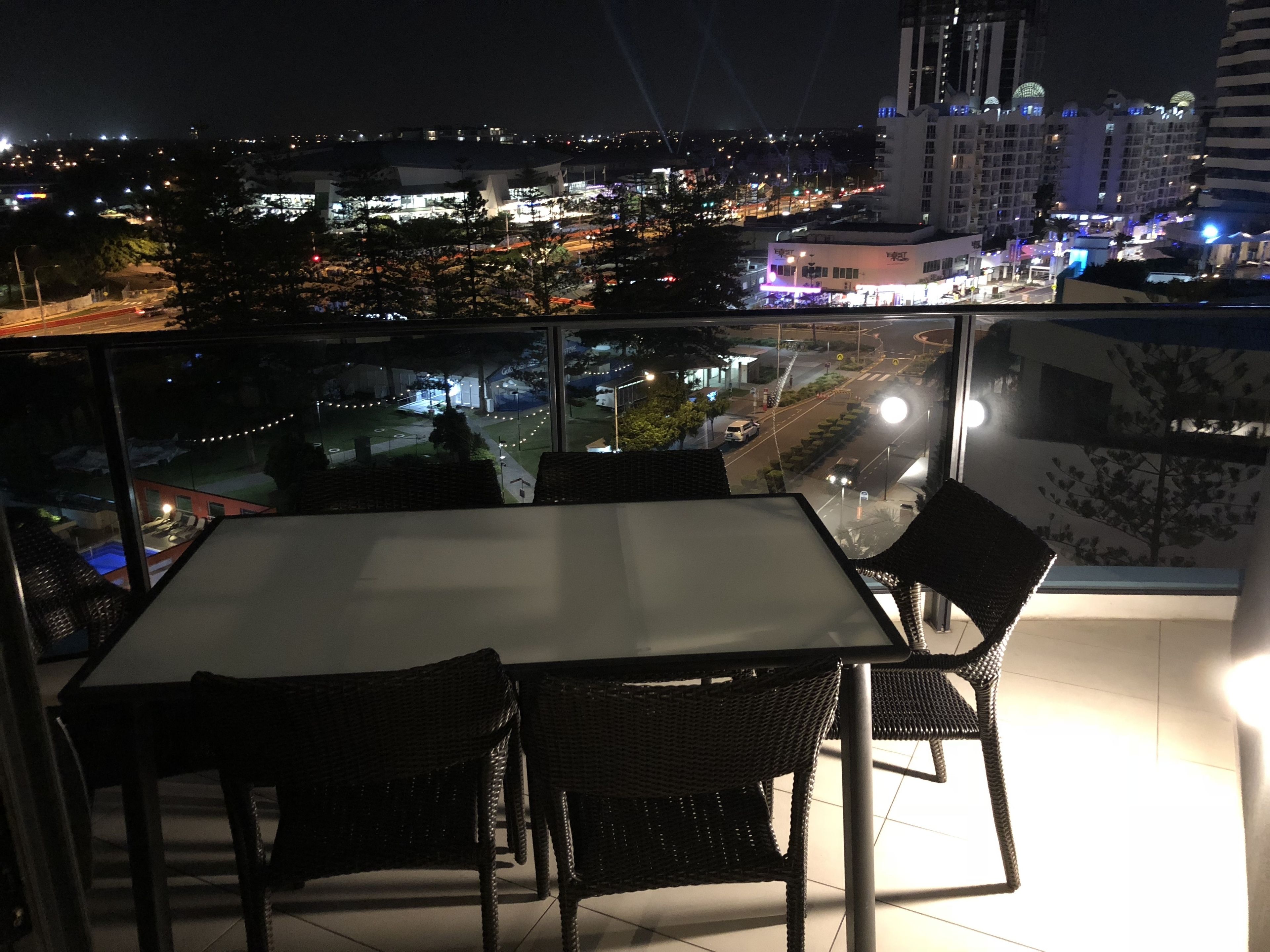 A balcony with a table and chairs, overlooking a cityscape at night.