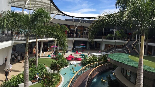 A multi-level indoor atrium with a central pool, palm trees, and various seating areas. - Large Apartment at Oracle Resort (Broadbeach)