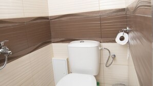 Pieni kylpyhuone, jossa on wc, roskakori ja suihkupää.