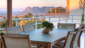 A dining area with a table and chairs, a potted plant, and a view of mountains and a cityscape. - Summer Breeze House * with private pool * private parking * (Χανιά)