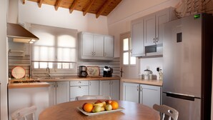 A modern kitchen with white cabinets, a stainless steel refrigerator, and a wooden dining table with fruit. - Summer Breeze House * with private pool * private parking * (Χανιά)