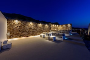 A modern outdoor lounge area with stone walls and contemporary furniture, featuring built-in lighting and a view of the surrounding landscape.