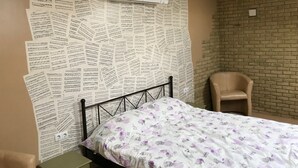 A bedroom with a bed, a chair, a small cabinet, and a brick wall. - Guest House near Kiev  (Софиевская Борщаговка)