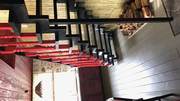 A staircase with a black metal railing and red accents, leading to a room with a wooden floor and a visible window. - Guest House near Kiev  (Софиевская Борщаговка)