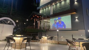 A building named "Euphoria Grand" with outdoor seating and a large screen displaying a cricket match. - The Euphoria Grand (Shimla)